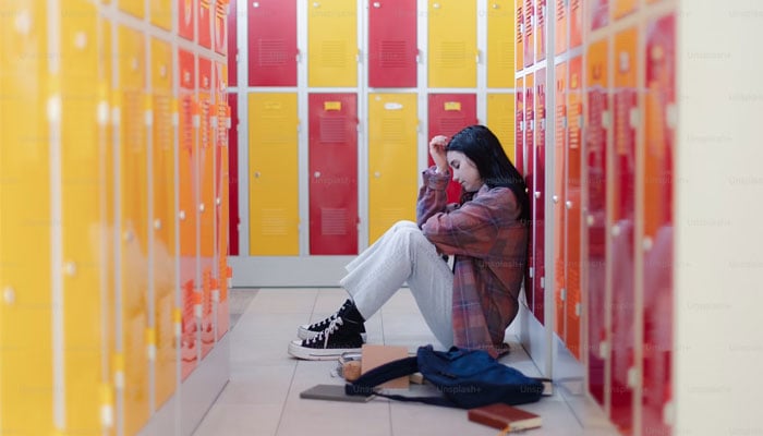 A young girl sits next to lockers in a school. — Unsplash